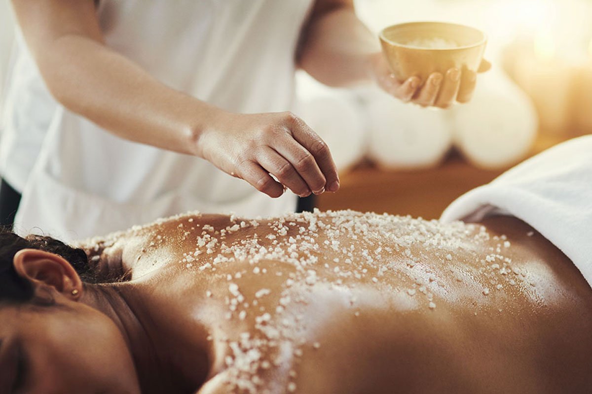 Woman, hands and salt in massage at spa for skincare, exfoliation or body treatment at resort. Hand of masseuse applying salts to back skin for relaxation, therapy or zen in healthy wellness at salon.